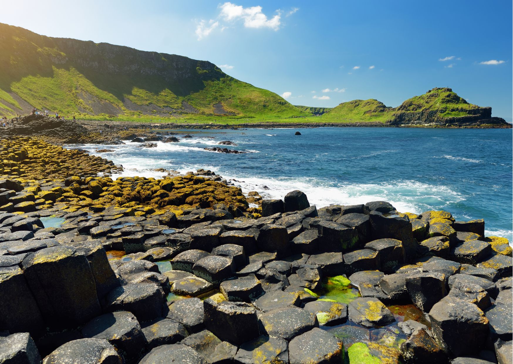 The hexagonal basalt columns of the Giant's Causeway on the Antrim coast of Northern Ireland, with waves crashing in the background.