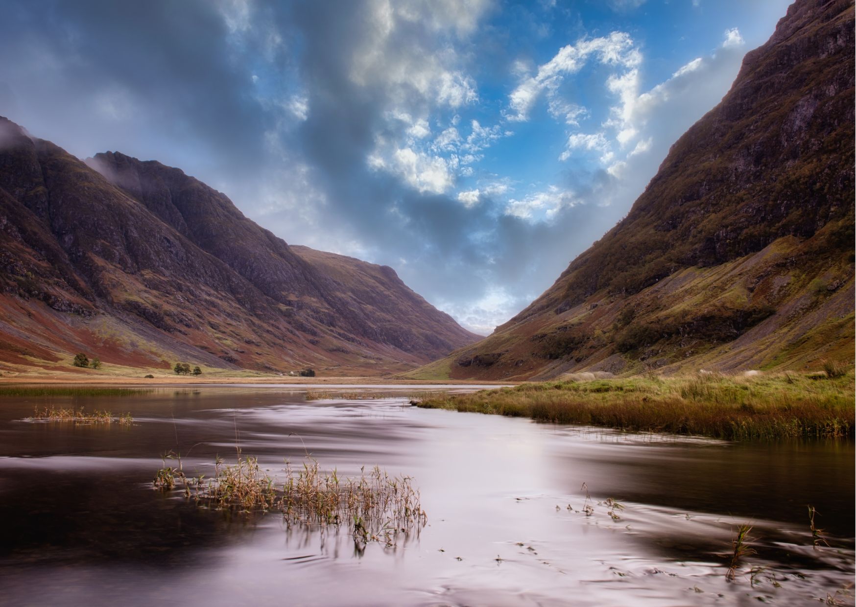 Serene loch nestled in the rugged landscape of Glencoe, Scotland, surrounded by steep mountains and cloudy skies.